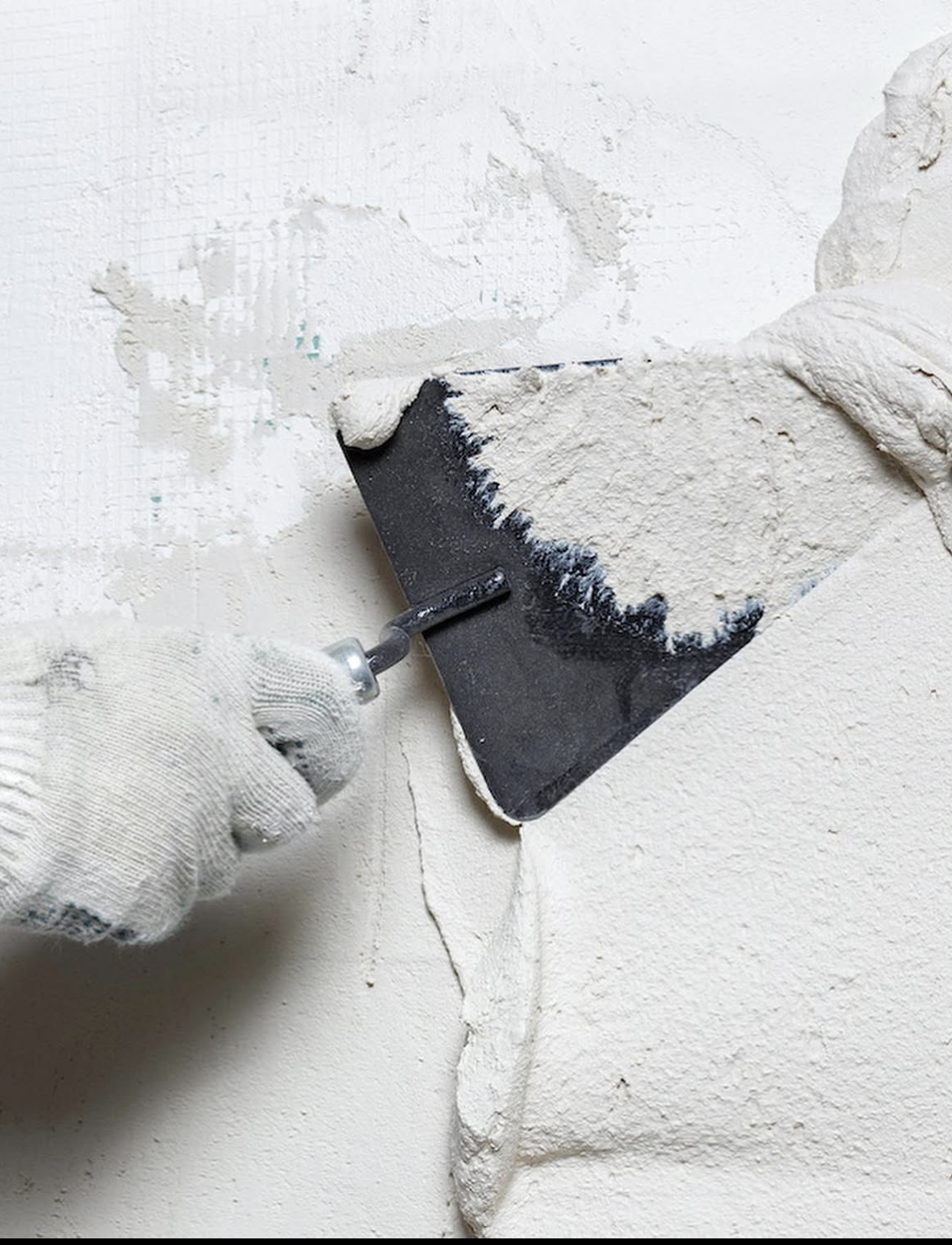 Gloved hand smoothing fresh plaster onto a wall with a trowel